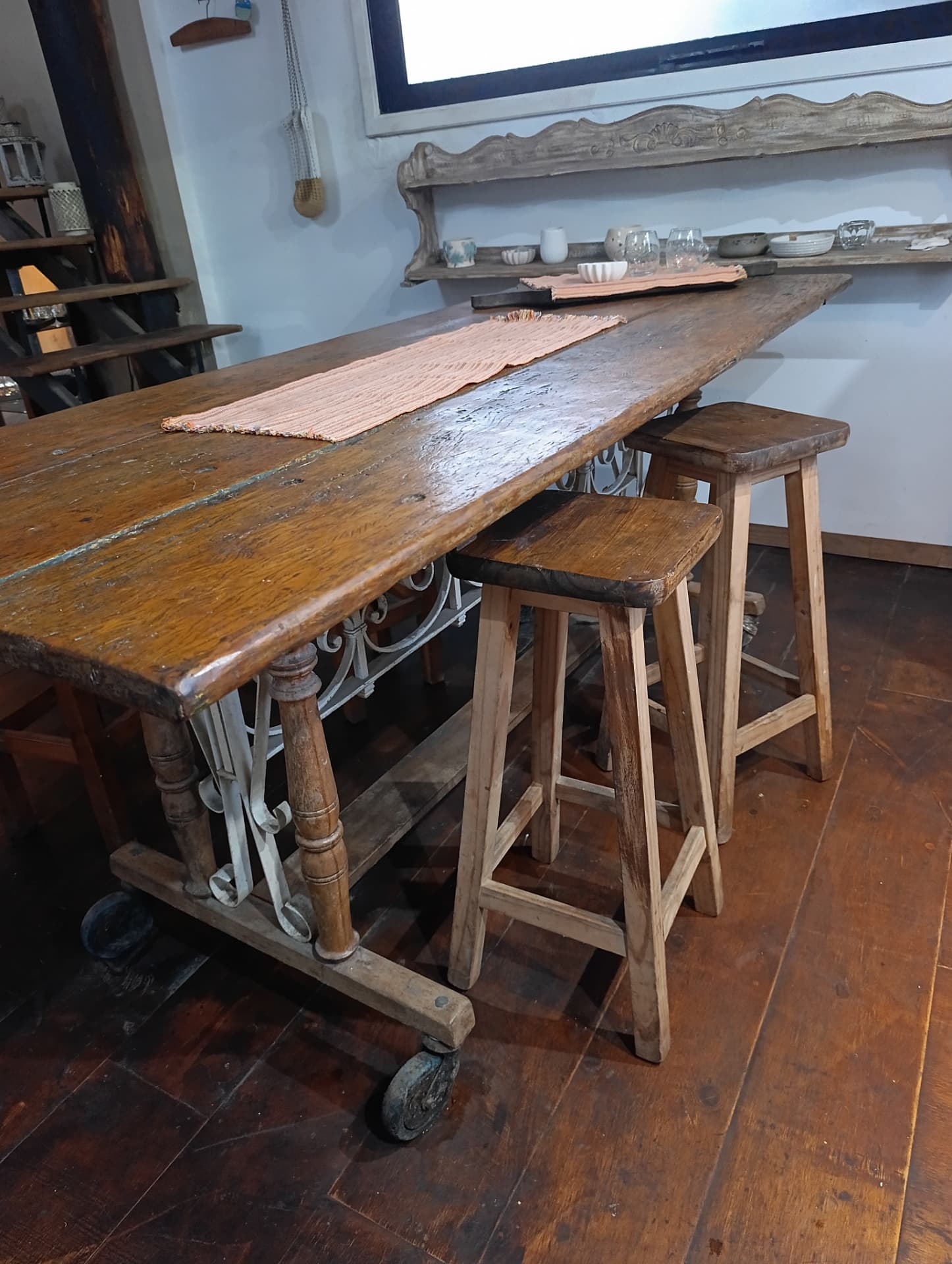 Interior rústico con mesa de madera larga sobre ruedas de hierro y banquetas altas