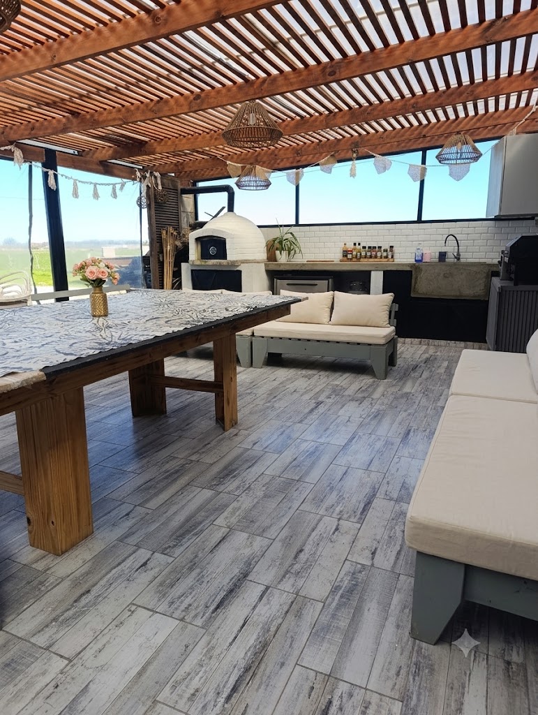 Quincho techado con mesa grande, horno de barro y sillones con almohadones beige